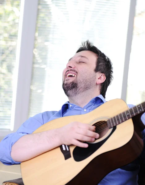 Uomo che suona la chitarra e canta al coperto sul divano — Foto Stock