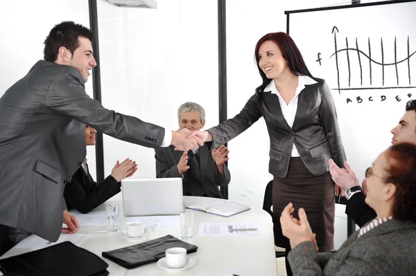 Zakelijke partners schudden handen na maken deal terwijl hun mede-werkers applaudisseren — Stockfoto