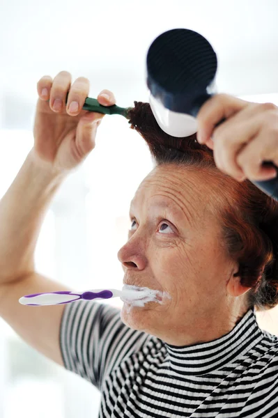 Eldre kvinne som tørker hår med vifte og pusser tenner – stockfoto