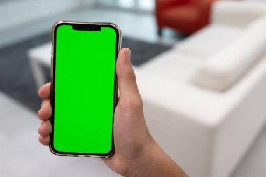 Modern oturma odasını, boş yeşil ekranlı cep telefonuyla akıllı bir ev vasıtasıyla verin.