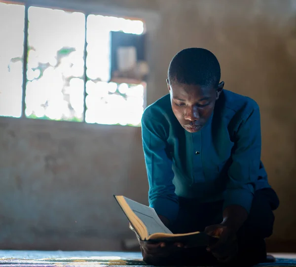 Afrykański nastolatek siedzi i czyta książki w biednej szkole — Zdjęcie stockowe
