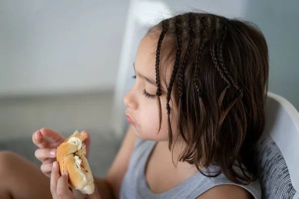 Menino comendo sanduíche enquanto sentado na mesa na cozinha — Fotografia de Stock