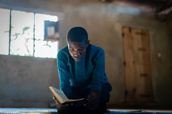 Afrykański nastolatek siedzi i czyta książki w biednej szkole — Zdjęcie stockowe