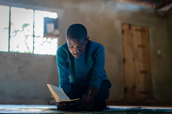 Afrikanischer Teenager sitzt und liest Buch in armer Schule lizenzfreie Stockfotos
