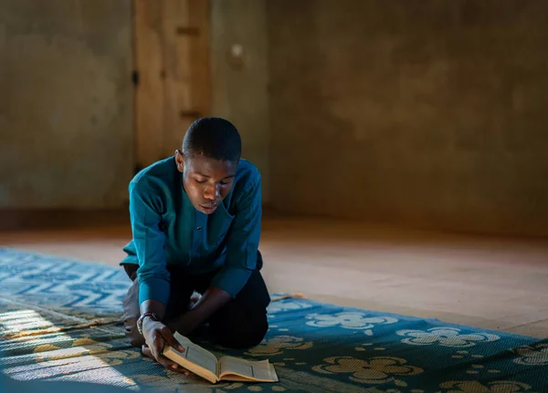 African teenage boy sitting and reading book in poor school — Stock Photo, Image