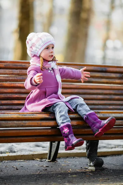 Νεαρό κορίτσι που κάθεται σ ' ένα ξύλινο παγκάκι — Φωτογραφία Αρχείου