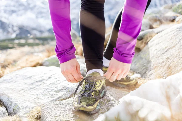 Female runner tying sports shoe in mountains on trail — Stock Photo, Image