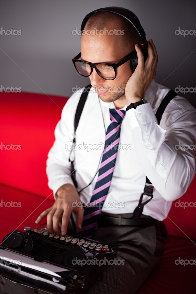 Young man listening music with headphones and working on an old typewriter