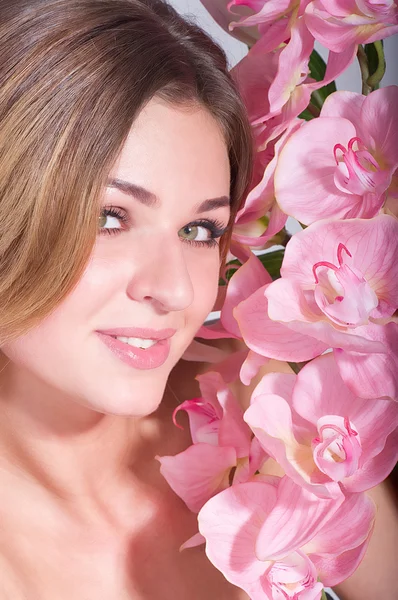 Beauty face of the young woman with pink orchid on background — Stock Photo, Image