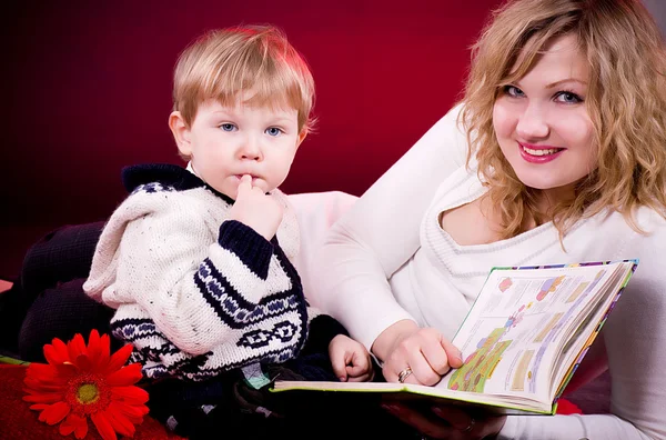Mother and baby boy reading book and smiling on red background — Stock Photo, Image