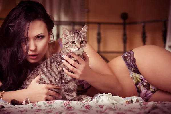 Привлекательная женщина в нижнем белье лежит на кровати с милой серой кошкой — стоковое фото