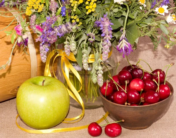 Fältet blommor, grönt äpple och körsbär i en tallrik — Stockfoto