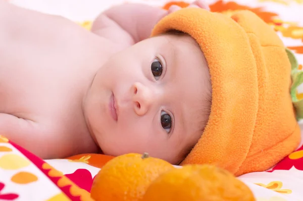 Новорожденная девочка в оранжевой шляпе с мандарином — стоковое фото