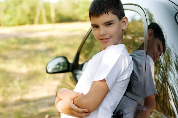 Pojken står nära en svart bil — Stockfoto