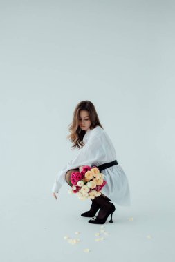 Bir buket gülü olan güzel bir manken kız. Aydınlık arka planda Spring Lady. Kadın vücudu ve tarz kavramı. Reklam ya da kıyafet satışı tasarımı. Metin boşluğu