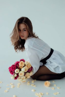 Bir buket gülü olan güzel bir manken kız. Aydınlık arka planda Spring Lady. Kadın vücudu ve tarz kavramı. Reklam ya da kıyafet satışı tasarımı. Metin boşluğu