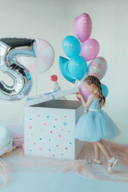 Mavi elbiseli sevimli, gülümseyen küçük kız. İyi ki doğdun Doğum günü prensesi bir balon zeminine karşı pastayla. Hediyelik eşya dükkanı. Alışveriş günü. Çocukluk ve komik kutlama konsepti.