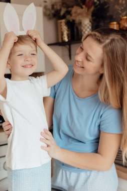 Kartondan yapılmış tavşan kulaklı mutlu çocuk. Paskalya Tavşanı Anne ve Çocuk olarak Paskalya bayramını evde birlikte kutluyoruz. Şükran Günü gelenekleri ve çocukluk birlikteliği kavramı. Tatil gelenekleri. Kutlama ve sevinç konsepti.