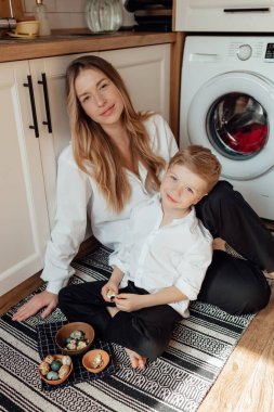 Mutlu aile paskalya yumurtalarını içeride hazırlıyor. Anne ve çocuk evde birlikte mutlu Paskalya tatili kutluyorlar. Şükran Günü gelenekleri ve çocukluk birlikteliği kavramı. Tatil gelenekleri. Kutlama ve sevinç konsepti.