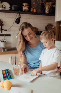 Anne ve küçük çocuk Paskalya bayramı için bir kartpostal hazırlıyorlar. Evde birlikte Paskalya tatili. Şükran Günü gelenekleri ve çocukluk birlikteliği kavramı.