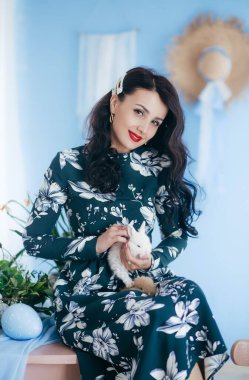 Paskalya günü, tüylü tavşanı olan ve içeride hoplayıp zıplayan genç ve güzel bir kadın. Çiçekli bir kızın moda portresi. Mutlu Paskalyalar ve bayramlar..