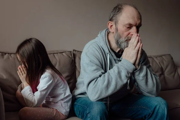 Ukrainian worried middle aged hoary man supporting little frightened grandgirl. Unhappy mature older grandfather with little girl at home. Concept of stress and fear