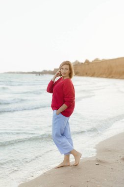 Kumsalda esintiyi hisseden mutlu olgun bir kadın. Sahilde orta yaşlı güzel bir kadın. Orta yaşlı kadın kendini iyi hissediyor ve denizde özgürlüğün tadını çıkarıyor..