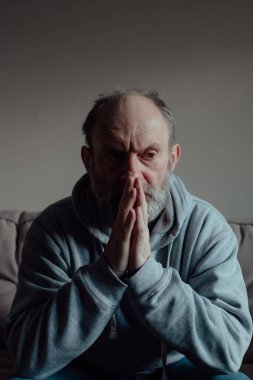 Ukrainian worried middle aged man folded his hands in prayer and thinks intently. Unhappy mature older grandfather at home.