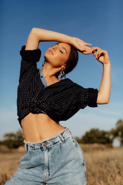 Fashionable young model in boho style clothes on a background of dry grass, field. Female beauty and style concept. Advertisement or clothes sale design.