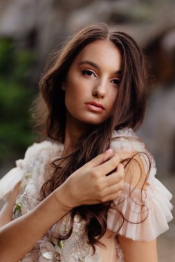 Fashionable young model in boho style dress on a background of rocks. Female beauty and style concept. Advertisement or clothes sale design.