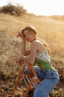 Fashionable young model in boho style clothes on a background of dry grass, field. Female beauty and style concept. Advertisement or clothes sale design.