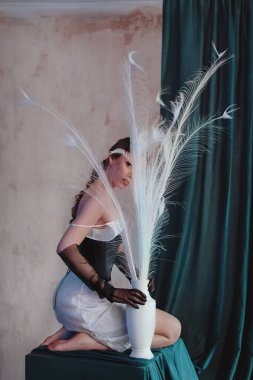 Fashion Portrait of stylish girl with white feathers. Beautiful model European girl posing in a casual clothes in the studio. Female body and style concept.