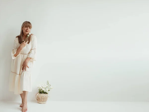 Красива Літня Жінка Квітами Вона Носить Легкий Одяг Білому Тлі — стокове фото