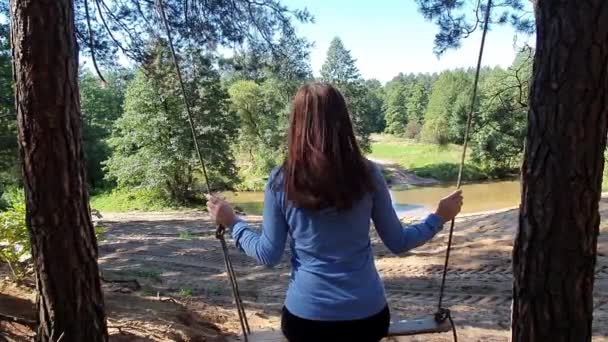 Jeune belle femme se balançant sur une balançoire en bois suspendue par corde sur une branche d'arbre — Video