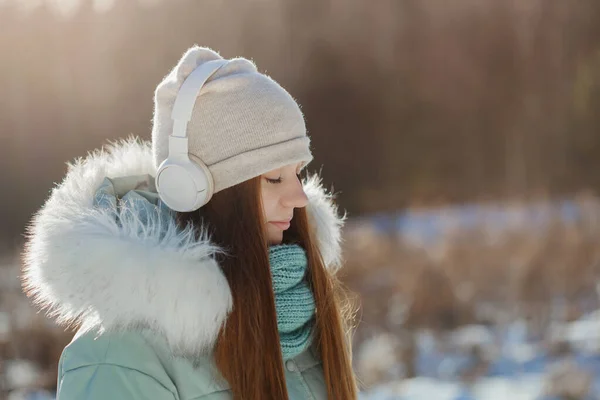 Foto de alegre joven sonriente feliz con auriculares en el parque de invierno con los ojos cerrados en los sueños y la calma completa — Foto de Stock