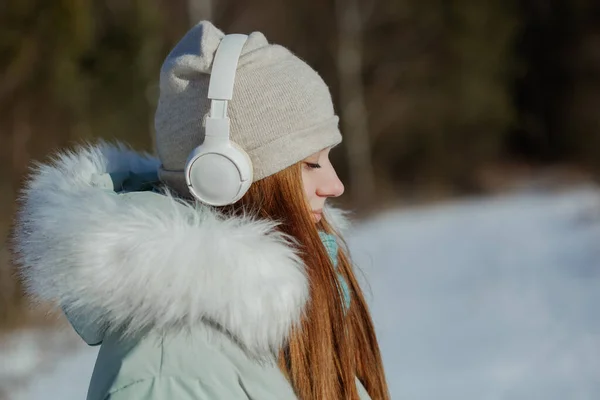 Photo de joyeux heureux jeune fille souriante avec écouteurs dans le parc d'hiver avec les yeux fermés dans les rêves et le calme complet — Photo