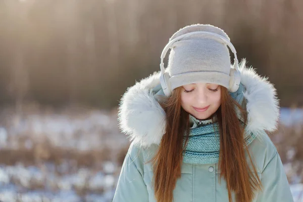 Foto av glad glad ung leende flicka med hörlurar i vinterparken Stockbild