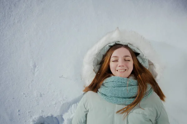 Νεαρή χαμογελαστή όμορφη κοπέλα βρίσκεται στο χιόνι ευτυχισμένη και ικανοποιημένη με τη ζωή Εικόνα Αρχείου