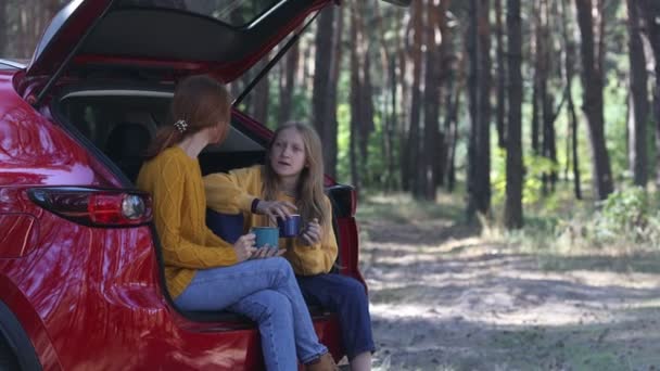オープンカーのトランクに座って松の森の道で自然を楽しみお茶を飲む母親と娘の森のピクニック — ストック動画