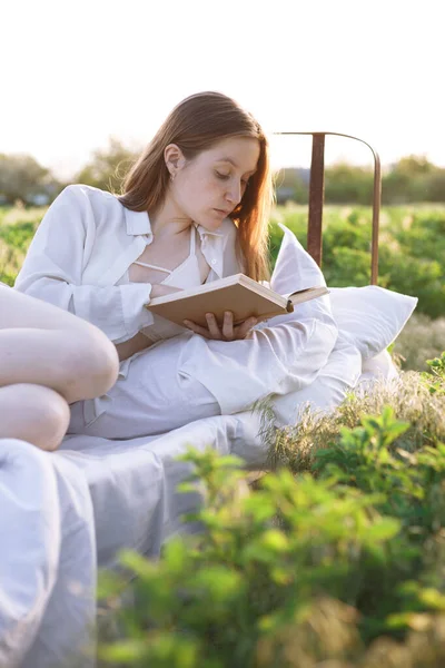 Κορίτσι Που Διαβάζει Ένα Βιβλίο Στο Κρεβάτι Ανάμεσα Στα Χωράφια — Φωτογραφία Αρχείου