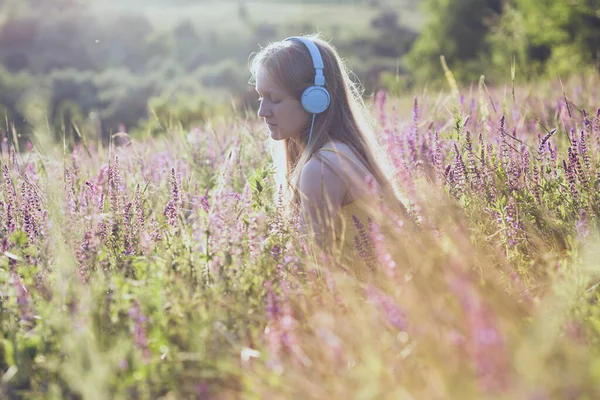 戴耳机的快乐微笑的女孩在夕阳背景上听音乐 照片出福库 — 图库照片