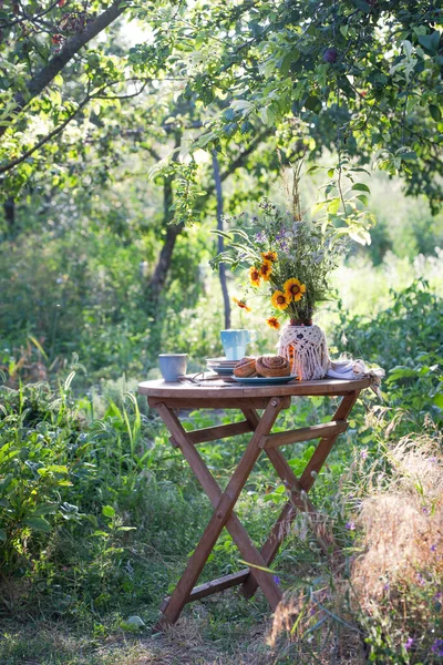 田舎風の庭とお茶会 静物画 シナモンロール カップ 皿と野花の花瓶 — ストック写真