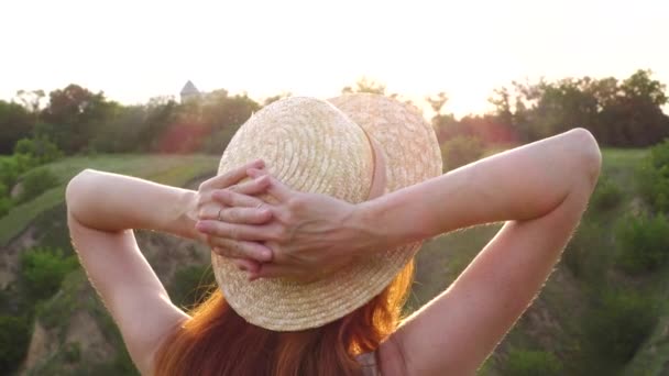 穿着草帽站在黄昏的草地上 被夕阳西下的光芒照亮的女孩的后视镜 — 图库视频影像