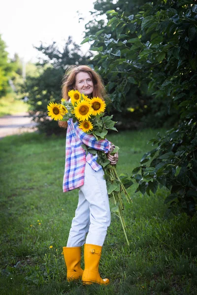 girl holding a huge bouquet of sunflowers in their hands against the backdrop of a rural landscap