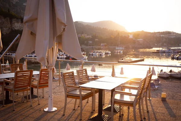 ウォーターフロントのカフェだ 空のテーブルと椅子と背景にボートがある湾 — ストック写真