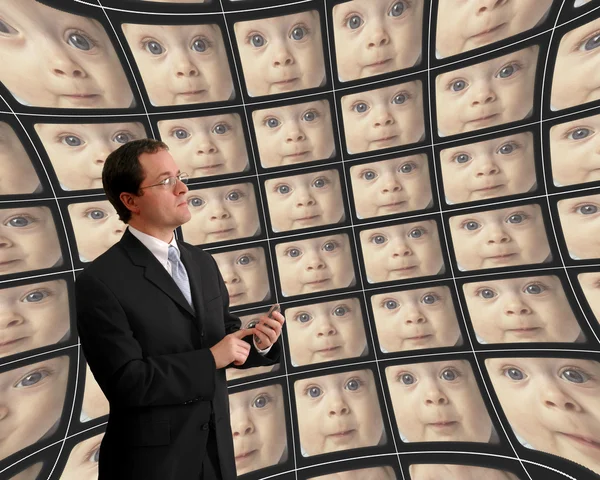 Man in suit monitoring babies on distorted video screens — Stock Photo, Image