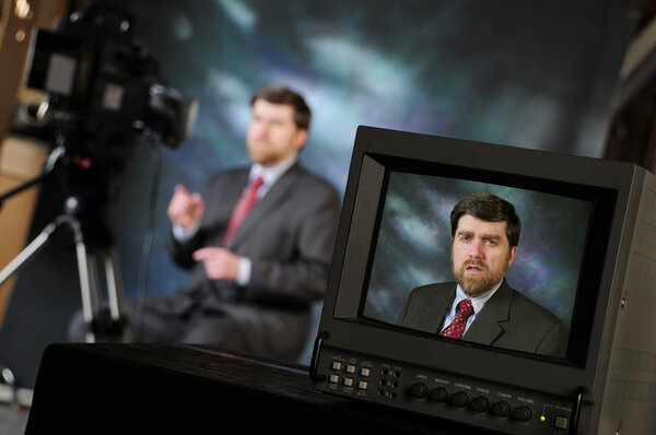 Monitor in production studio showing man talking into a televisi