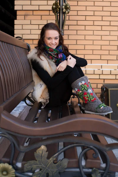 Девушка сидит на скамейке на фоне бревенчатой хижины — стоковое фото