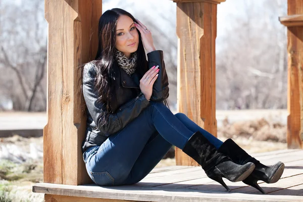 Young brunette woman sitting leaning against a wooden post — Stock Photo, Image