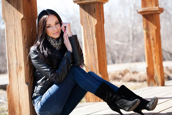 Jonge brunette vrouw vergadering leunend tegen een houten post — Stockfoto